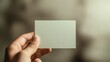 © Johannes - Artistic macro of a blank card in pale sage green, delicately held between fingers, softly blurred taupe backdrop, elegant soft lighting for a clean professional look.