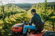 Farmer mowing between fruit trees in his orchard.