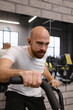 © arthurhidden - Man wearing a white shirt intensely exercising on an air bike at the gym.