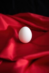 Poster - Delicate white egg sits gracefully atop rich red fabric creating a striking contrast. The smooth surface of the egg reflects soft light enhancing its subtle beauty.