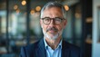 © Vadym - Close-up portrait of mature businessman in modern office setting. Successful business man wearing glasses looks directly at camera. Pro appearance conveys confidence, expertise in leadership.
