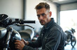 © Vadym - Young mechanic repairs motorcycle in garage. Man fixes motorbike engine, working with tools, looking at camera. Service, maintenance, pro repair, bike repair shop.