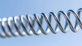 Closeup of metal spring stretched to its limit with smooth shiny surface against soft blue background, showing tension and flexibility in coil design