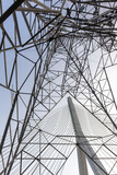 Creative architectural composition showing part of Flintshire Bridge, a modern cable-stayed structure in North Wales, framed by the geometric lattice of a towering electricity pylon