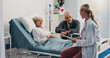 © Wesley25/peopleimages.com - Healthcare, doctor and old couple in clinic, conversation and recovery for cancer treatment. Illness, medical emergency or senior woman in bed, elderly man and consultation with documents and talking