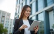 © car - Smiling asian businesswoman using digital tablet in front of modern office building. High quality