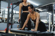 © Phimwilai - Determined asian woman performing bench push ups with personal trainer in gym