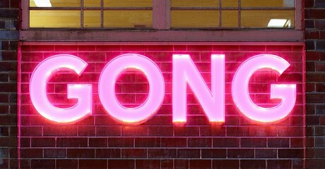 Aufkleber - Bright pink neon sign spells GONG against brick wall. Windows visible above lettering, dark background surrounds scene.