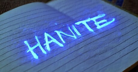 Aufkleber - Open notebook displays glowing word HANITE. Lines suggest handwritten text. Dark background emphasizes bright illumination.