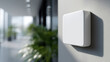 © Nakarin - Close up of white square smart device mounted wall modern office with blurred background of plants and windows, conveying clean and minimalistic design, possibly sensor or control panel