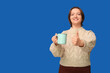 © Pixel-Shot - Young woman with mug of coffee showing thumb-up on blue background