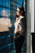 © BullRun - Confident businesswoman talking on smartphone beside office window