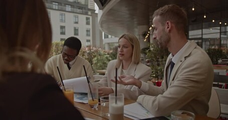 A diverse business team collaborates on a project at an outdoor cafe, reviewing documents and engaging in productive discussion.