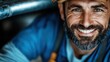 © Pinklife - A joyful middle-aged man with a beard and work attire smiles warmly as he poses in a workshop, embodying dedication and pride in his craft and profession.