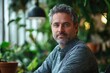© anura - Confident Casual Professional Man in Relaxed Greenery-Filled Coffee Shop Workspace with Natural Light and Potted Plants