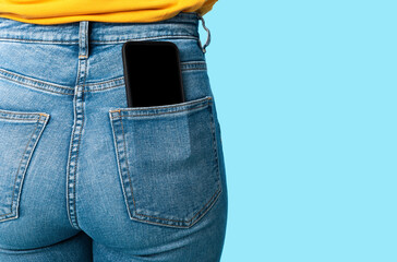 Poster - Cropped view of female having cellphone with blank screen in jeans pocket on blue studio background, mockup for mobile app or website. Free space for your advertisement template