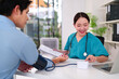 © snowing12 - Asian Woman Doctor Checks Patient Blood Pressure With Smile During Consultation at Clinic Office for Healthcare Expertise