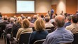 © An - A group of people sitting in a conference room, listening to a speaker.