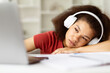 © Anastasiya - Bored or tired African American female student at home, leaning head on hand, wearing wireless headphones, looking tiredly at laptop screen, upset black woman feeling fatigue while study online