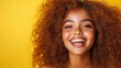 © Pinklife - A radiant young woman with curly hair and a warm smile stands in front of a vibrant yellow backdrop, embodying happiness and positivity in her expression and demeanor.
