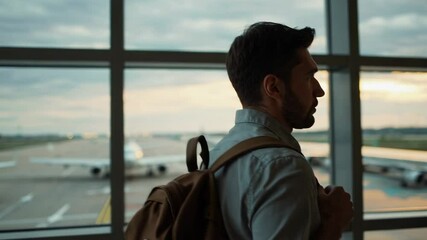 Aufkleber - Traveler wearing backpack walking through bright airport terminal, gazing at airplane silhouettes against golden sunset sky while contemplating upcoming journey