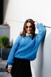 © nazariykarkhut - Stylish student wearing sunglasses and blue sweater is posing near white wall