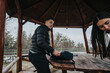 © qunica.com - Two individuals interact at a wooden picnic table on a cloudy day, enjoying nature and companionship. A wooden gazebo and surrounding trees set the natural outdoor scene.