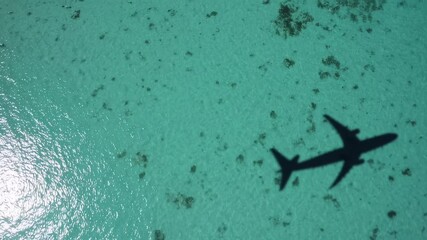Poster - Airplane shadow gliding over pristine turquoise waters alongside tropical island coastline, revealing breathtaking seascape with crystal clear ocean and scenic aerial perspective