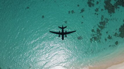 Aufkleber - Airplane shadow flying over beautiful turquoise ocean water near white sand beach and coral reef, creating a stunning tropical travel destination image