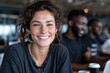 © Milos - A joyful woman with freckles smiles at the camera in a cozy workspace, representing positivity and engagement within a collaborative environment.