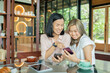 © sutlafk - two cheerful and beautiful girls are sitting together near the table and watching something on the phone. they look relaxed and happy. also girls are enjoying the time spending together.