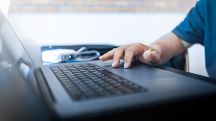 Close-up hand using laptop keyboard in modern office or coworking space. Ideal for business technology, typing, coding, online work, and data entry concepts.