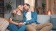 © VAKSMANV - Cute husband and gorgeous wife sitting on sofa hugging and cuddling, kissing together. Lovely couple of beautiful man and woman having great time at home in living room. Love concept.