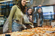 © PintoArt - Young women choosing pizza slices at pizzeria display window