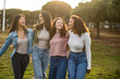 © PintoArt - Four young women walking together in a park, embracing friendship and diversity