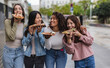 © PintoArt - Four young women eating pizza slices outdoors in urban setting