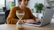 © Volha - Adult woman working on laptop with hourglass on desk in office