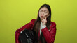 © Krakenimages.com - Woman pondering holding helmet in red jacket against vibrant yellow background showing thoughtful expression.