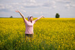 © kazakova0684 - Woman in bucket hat raising arms up, enjoying a warm summer day in a blooming yellow rapeseed field