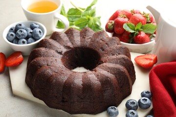 Wall Mural - Tasty chocolate bundt cake, tea and berries on light table, closeup