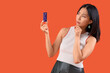 © Pixel-Shot - Thoughtful young beautiful Asian woman with credit card on orange background