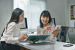 © Crystal - Two young Asian businesswomen happily working together with calculator and documents in modern office