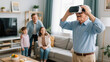 © AgungKY - Elderly man enjoying VR headset experience with young family looking him at family room