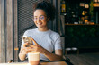 © Dusan Petkovic - Portrait of happy interracial girl sitting in cafe and typing messages on cellphone while smiling at it.