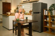 © saltdium - An elderly Asian woman sits cheerfully at the kitchen table, enjoying a homemade sandwich with salad and drink in a modern home setting, A relaxed morning routine