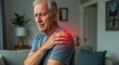 © Pics_With_Love - Senior Caucasian man sitting at home with hand on shoulder showing signs of pain and discomfort, red glow indicating musculoskeletal or cardiac condition