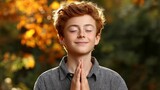 Young boy with closed eyes and folded hands practicing prayer outdoors in autumn