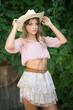 © iancucristi - portrait of a young beautiful woman framed by lush green foliage with hat of cowboy ,captured in a natural outdoor setting.. Woman dressed in a light pink off-shoulder top and short skirt posing