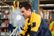 © yuttapon - Tired adult male warehouse worker with light skin wearing yellow uniform jacket sitting and resting during break. Exhausted expression after heavy work shift inside industrial storage environment.