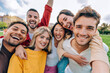 © Davide Angelini - Multiracial friends taking selfie picture with smart mobile phone outside - Group of young people smiling at camera outdoors - Friendship concept with guys and girls enjoying summer vacation